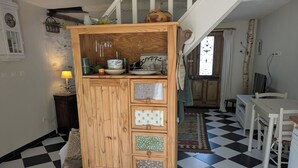 Une cuisine avec un carrelage à motifs, un meuble en bois doté de tiroirs, une lampe suspendue et une horloge au mur.