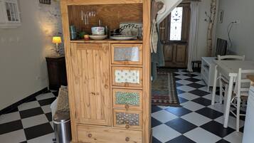 Een keuken met een geruit vloertje, een houten kast met lades, een hanglamp en een klok aan de muur.