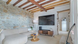 A living room with a stone wall, wooden beams, a sofa, a coffee table, a TV, and a guitar leaning against the wall. - Heated Plunge Pool | Mountain View’s (Málaga)