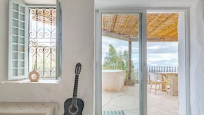 A room with a guitar, a bench, a window with metal bars, and a sliding glass door leading to an outdoor patio with a table and chairs. - Heated Plunge Pool | Mountain View’s (Málaga)