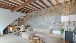 A cozy living room with a stone wall, wooden beams, a sofa, a dining table with chairs, and a lamp. - Heated Plunge Pool | Mountain View’s (Málaga)