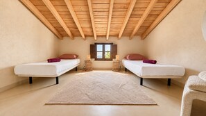 Een slaapkamer met twee bedden, een groot tapijt, houten balken in het plafond en een raam.