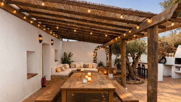 Eine Terrasse im Freien mit einem Holztisch und Bänken, einer überdachten Sitzgelegenheit und einer Steinmauer.