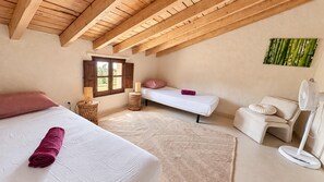 A bedroom with a large bed, a smaller bed, a sitting area, a window, and a fan. - Heated Pool | Villa with Mountain View (Málaga)