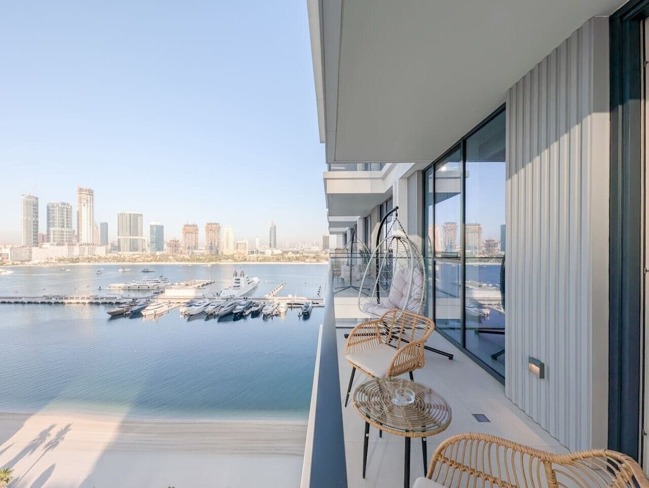 Ein Balkon mit Korbmöbeln, der auf einen Yachthafen und eine Stadtansicht blickt.