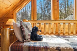 A cozy cabin room with a large window, a wooden deck, and a quilted bedspread. - The Toasted Turkey (Gatlinburg)