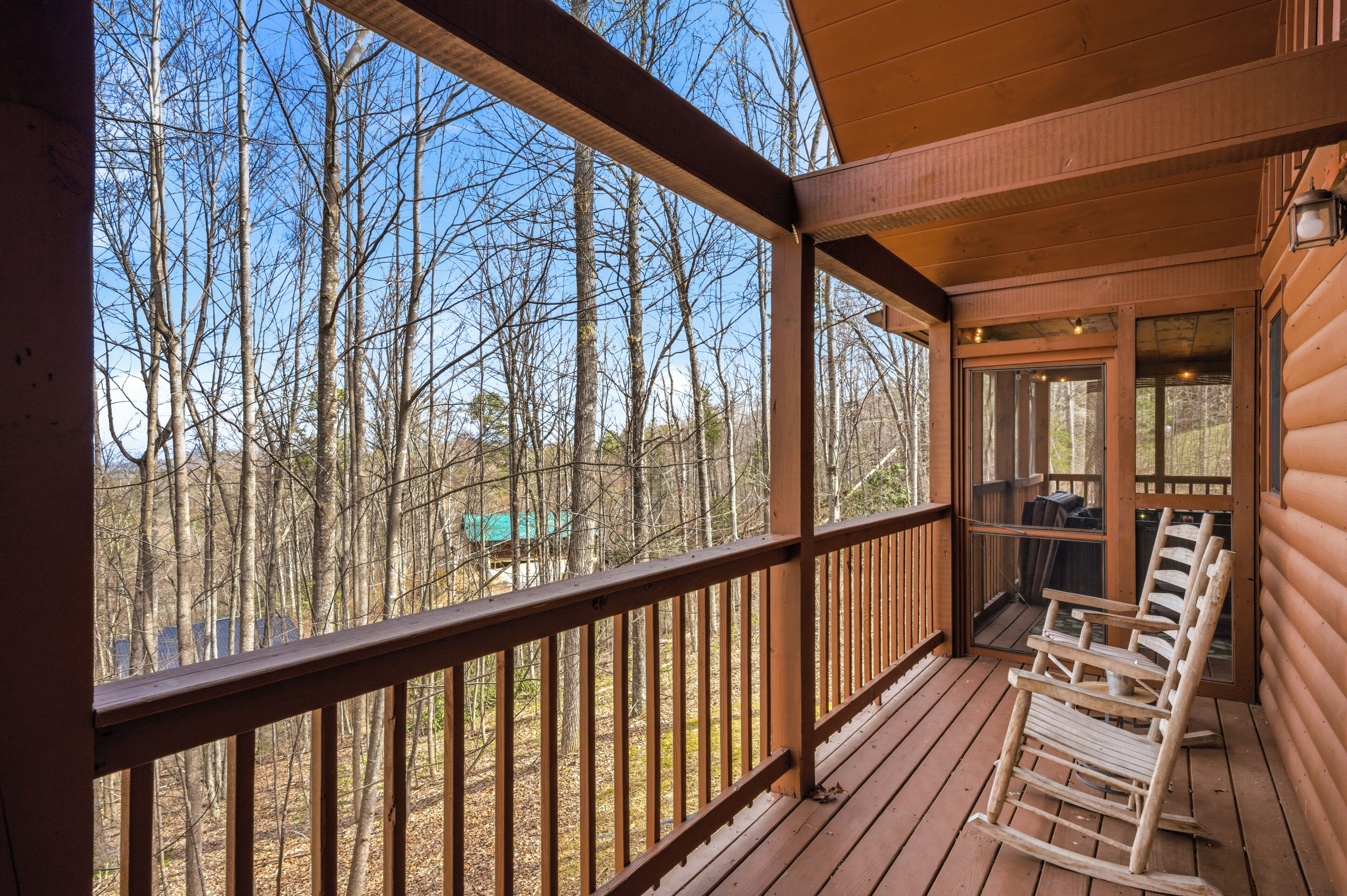 A wooden deck with a railing, a rocking chair, and a view of a forest.