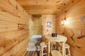 A wooden cabin interior with a round wooden table and stools, a framed picture on the wall, and a light fixture. - The Toasted Turkey (Gatlinburg)