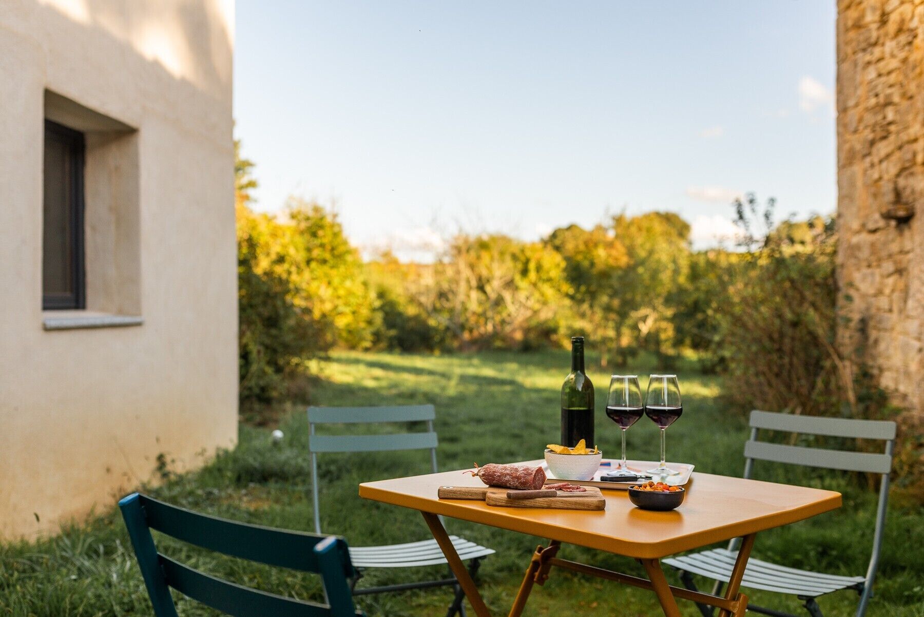 Mesa al aire libre con una botella, vasos y comida.