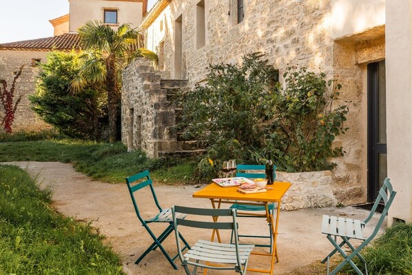 Un espace extérieur aménagé pour les repas, avec une table et des chaises, un chemin menant à un bâtiment et de la verdure.
