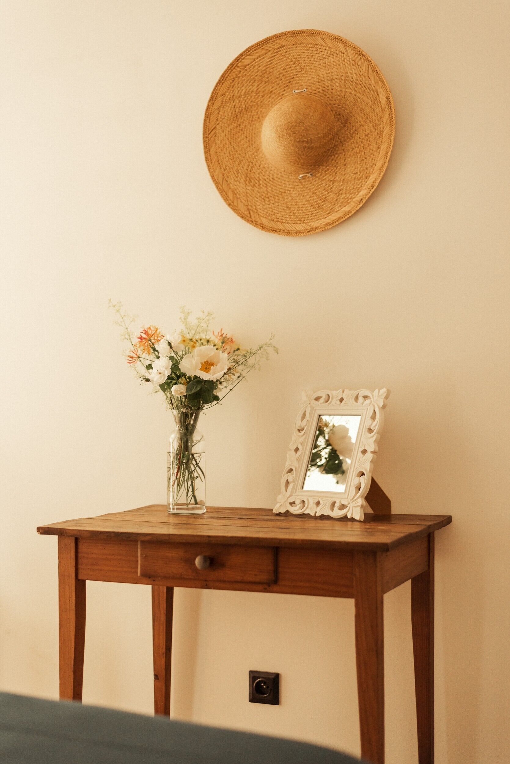 A wooden table with a vase of flowers and a framed mirror against a wall.