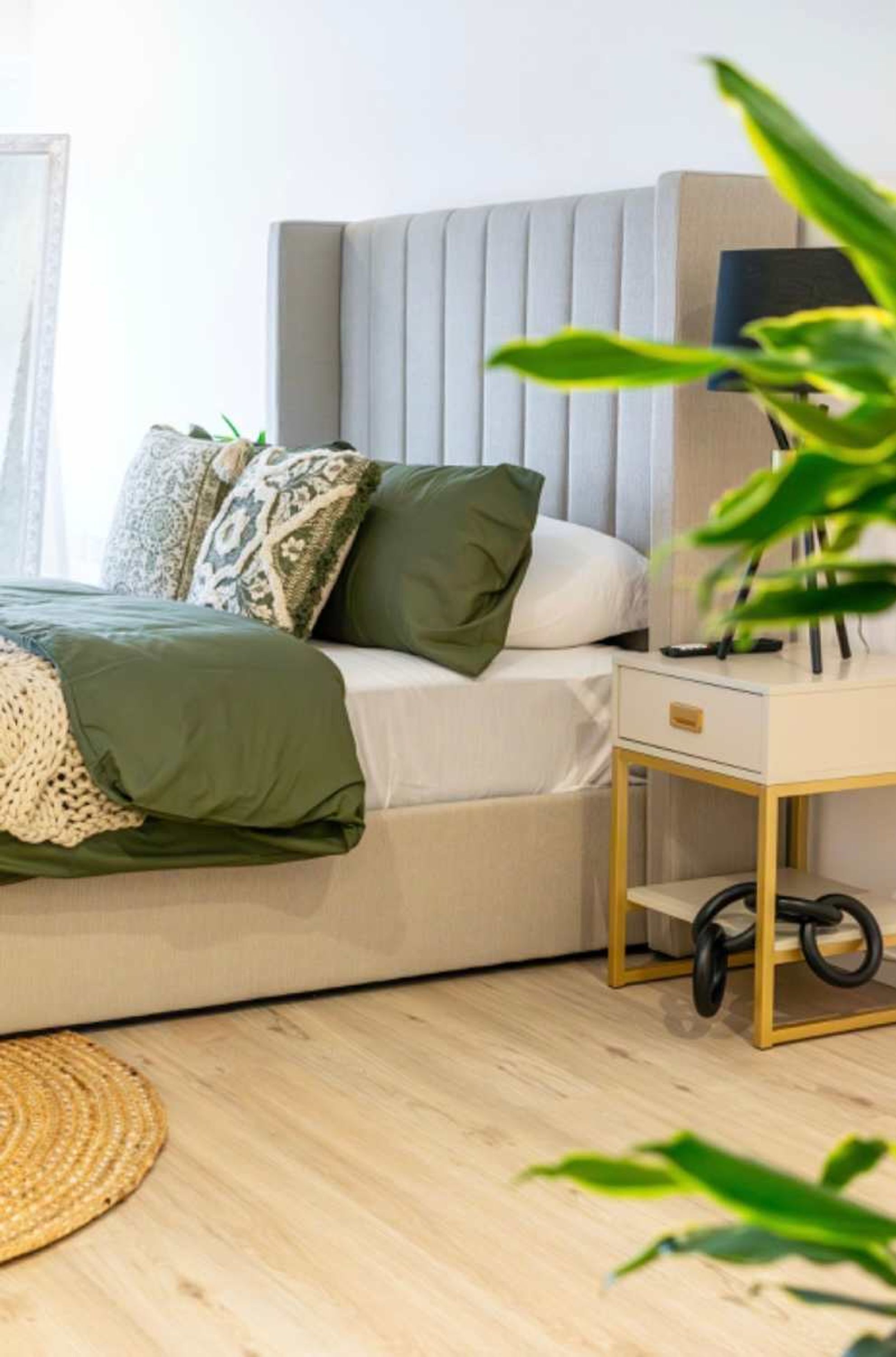 Un dormitorio moderno con una cama, mesita de noche, lámpara y una planta.