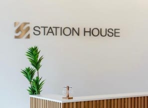 Un mostrador de recepción con un letrero que dice 'STATION HOUSE' y una planta en maceta a su lado.