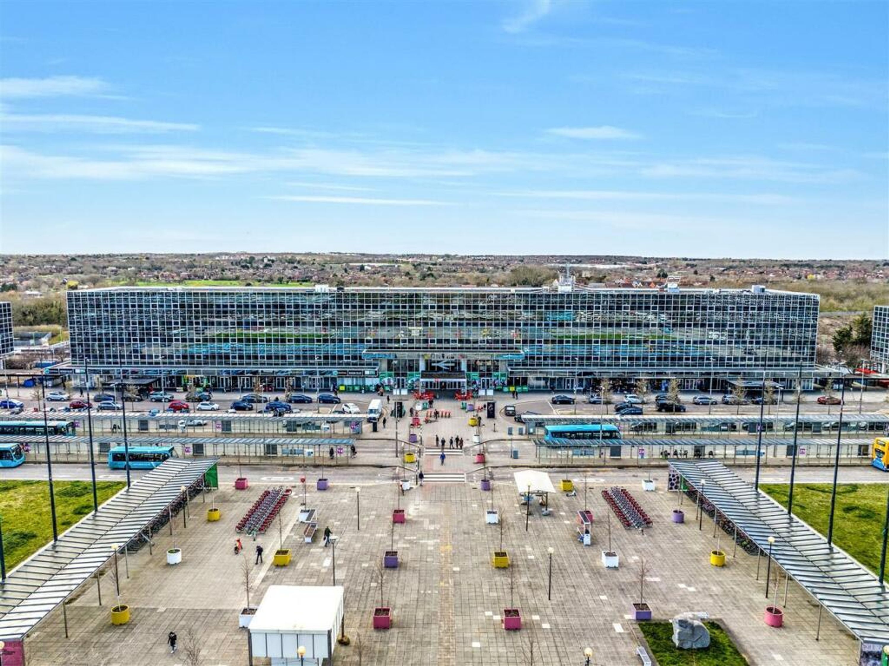 A modern building with a glass facade, a parking lot with several cars, and a clear sky.
