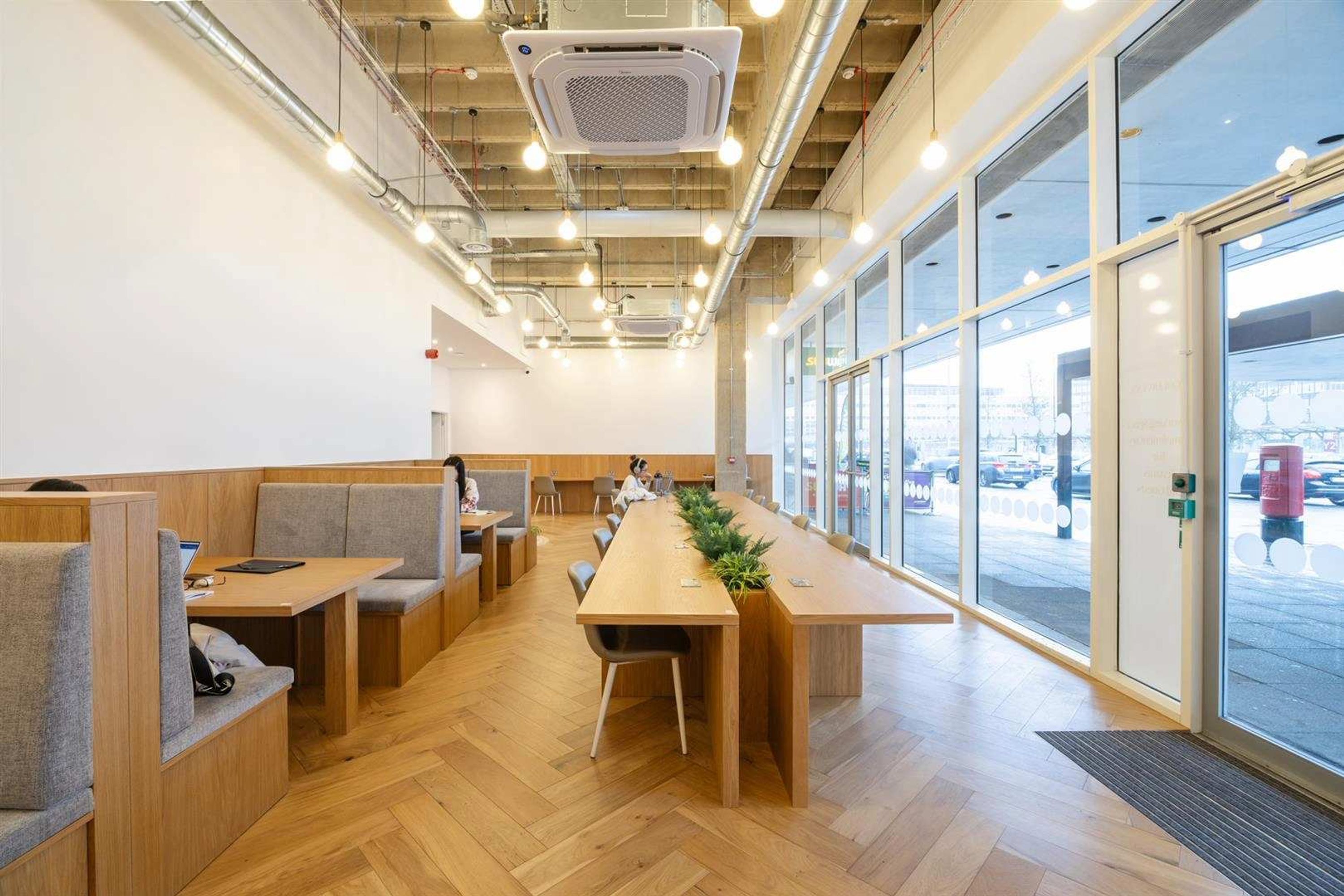 Un interior moderno con una larga mesa de madera, zonas de estar y ventanas amplias.