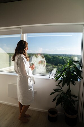 A person in a white robe standing by a window with a view of greenery outside. - Station Noir Stylish 1-bed in Central MK (Milton Keynes)