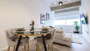 A modern living room with a glass dining table, two chairs, a sofa, and a TV mounted on the wall. - Station Noir Stylish 1-bed in Central MK (Milton Keynes)