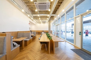 A modern interior with a long wooden table, seating areas, and large windows.