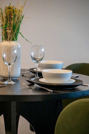 A dining table set with white bowls, a wine glass, and a vase with dried plants.