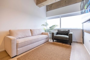 A living room with a sofa, armchair, small side table, and a potted plant.