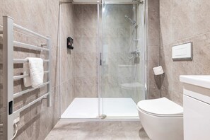 A modern bathroom with a glass-enclosed shower, a white toilet, and a towel rack with multiple towels. - Station Elan Sleek 2-bed Apartment in Central MK (Milton Keynes)