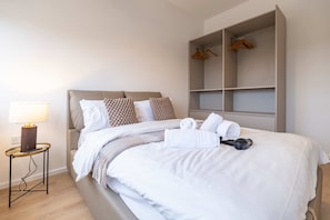 A neatly made bed with a headboard, a bedside table with a lamp, and a wardrobe with hanging space.