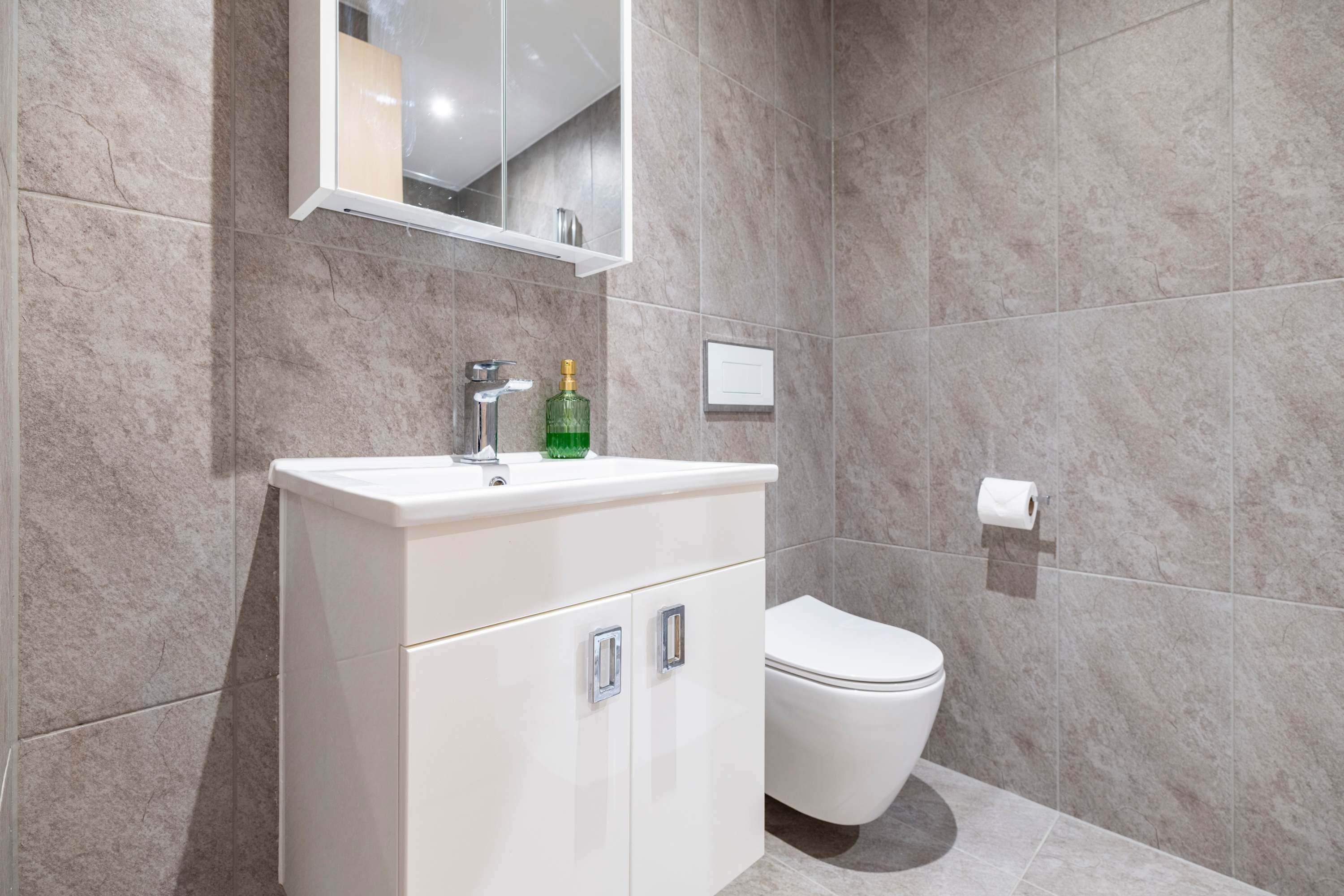 Et moderne badeværelse med en hvid kommode, toilet og spejl.