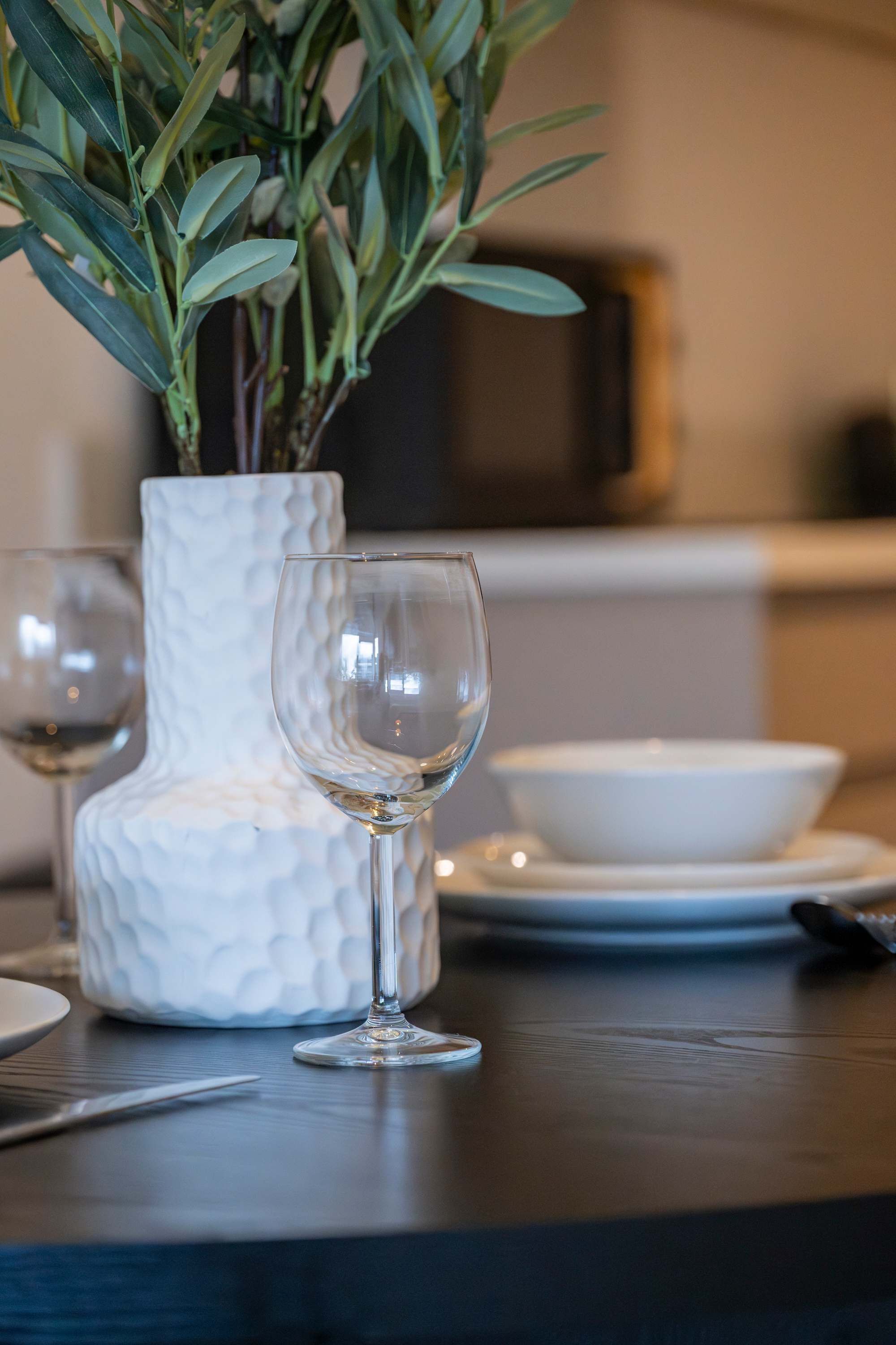 Une table sur laquelle se trouvent un vase blanc à texture particulière, deux verres à vin transparents et un bol blanc.