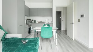 A modern, compact room with a bed, a dining table with chairs, a kitchenette, and a door leading to another room. - Entire Rental Unit in Linford Wood (Milton Keynes)