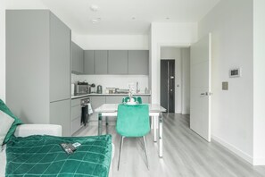 Una habitación moderna y compacta con una cama, una mesa de comedor con sillas, una kitchenette y una puerta que da a otra habitación.