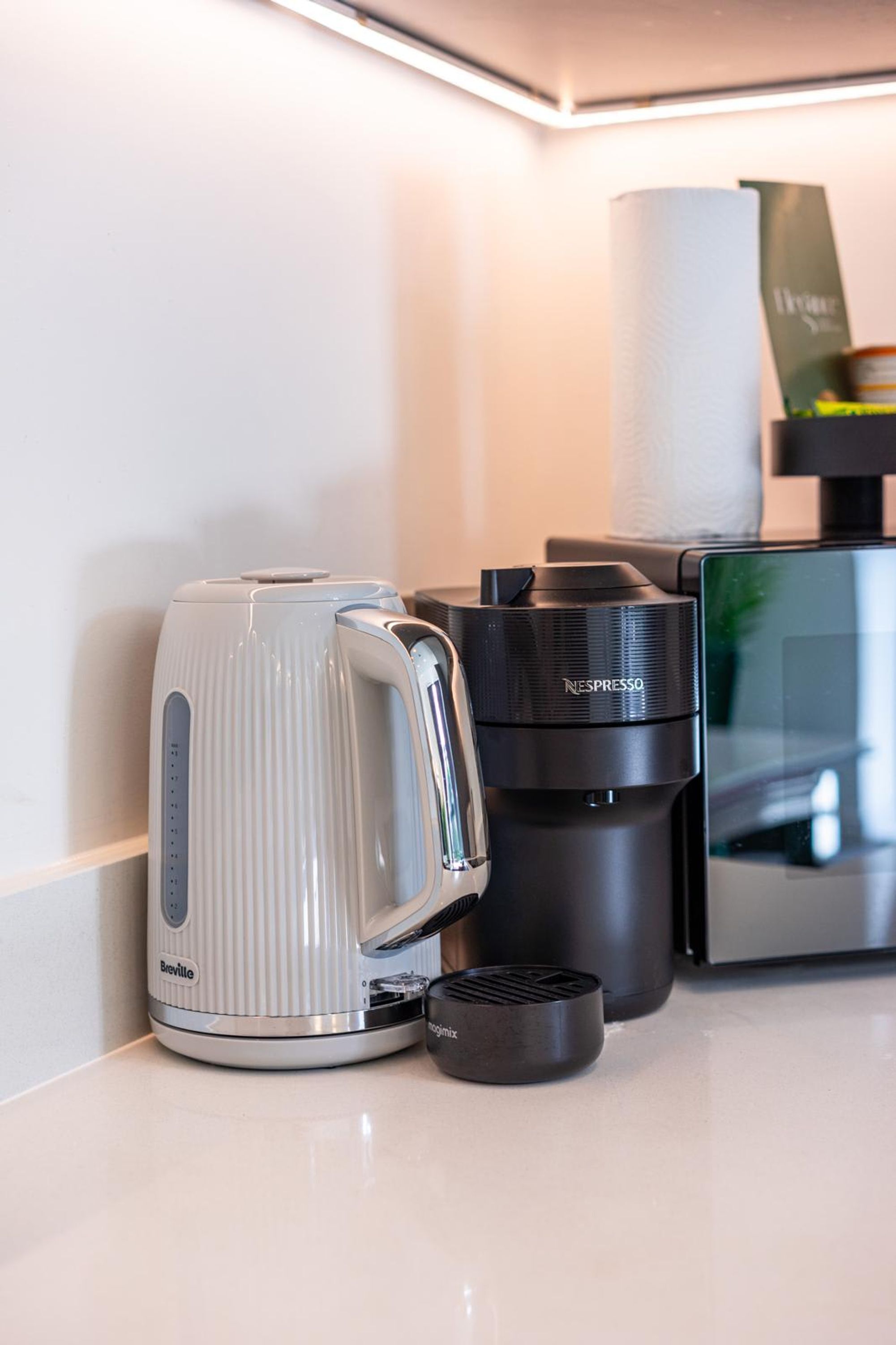 A Breville coffee maker, a Nespresso capsule machine, and a paper towel dispenser on a countertop.