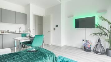 A modern bedroom with a bed, a desk, and a TV mounted on the wall.