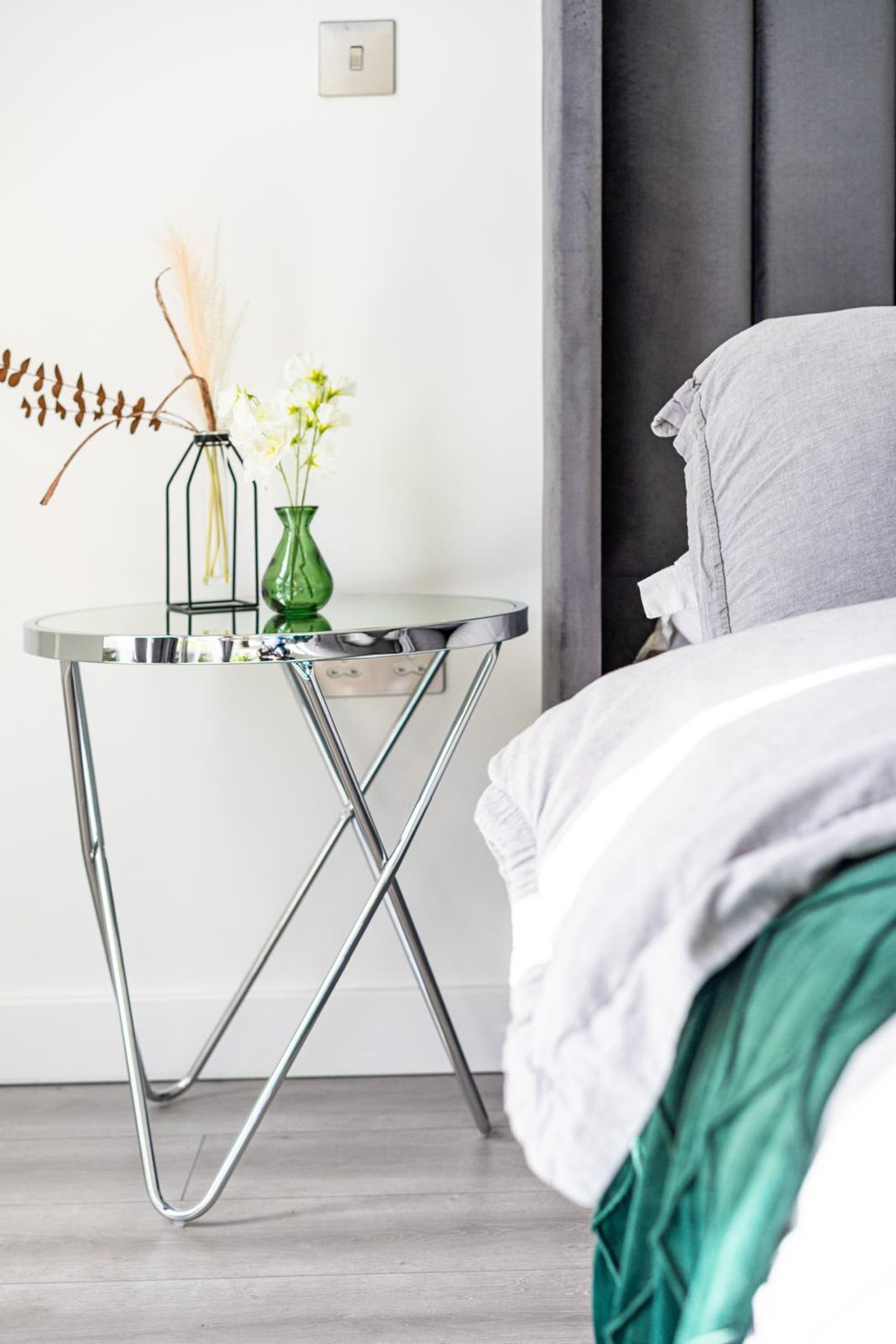 Un dormitorio moderno con una cama, una mesita de noche con un florero y un interruptor de luz.