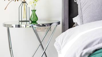 Un dormitorio moderno con una cama, una mesita de noche con un florero y un interruptor de luz.