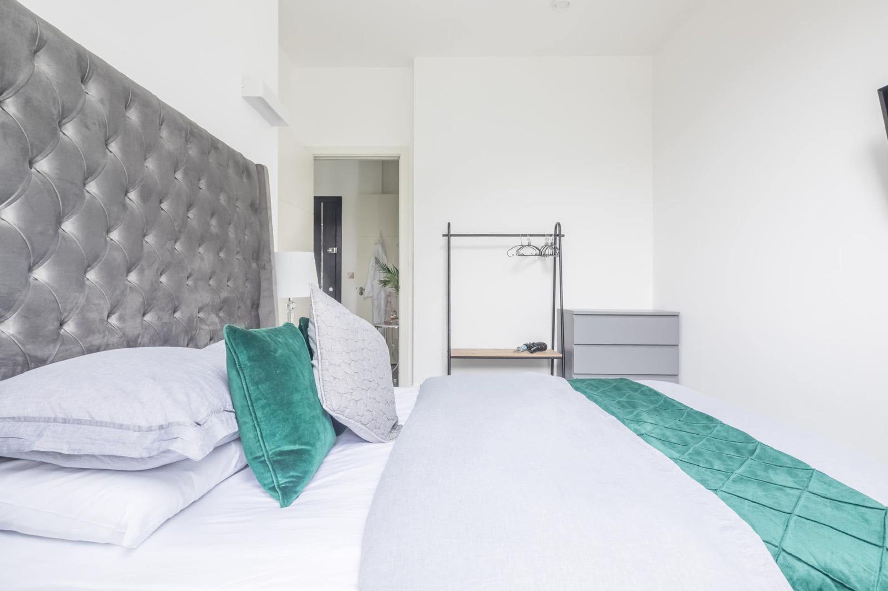 Een slaapkamer met een gestoffeerd hoofdeinde, een bed met wit en groen beddengoed, een nachtkastje en een kledingkast.