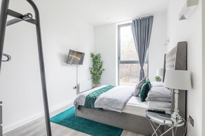 Una habitación de hotel moderna con una cama, un televisor, una ventana con cortinas, una planta y una lámpara.