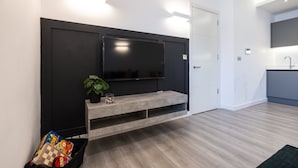 Moderni olohuone, jossa on litteänäyttöinen televisio, seinään integroitu penkki ja pieni kasvi.