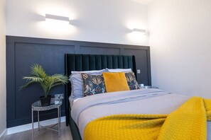 A modern bedroom with a dark headboard, a bed with patterned pillows, a small side table with a plant, and a bright yellow throw blanket. - Linford Luxe Quiet 1-bed Retreat in Milton Keynes (Milton Keynes)