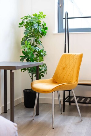 A yellow chair with a quilted backrest, a potted plant, a metal table, and a window with a black frame. - Linford Luxe Quiet 1-bed Retreat in Milton Keynes (Milton Keynes)