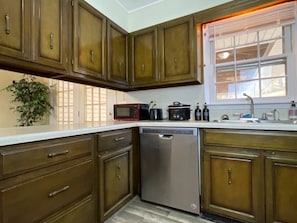A kitchen with wooden cabinets, a dishwasher, a microwave, and a window with blinds. - Spacious, Charming & Serene Family Haven ~ Parking (Kingsport)