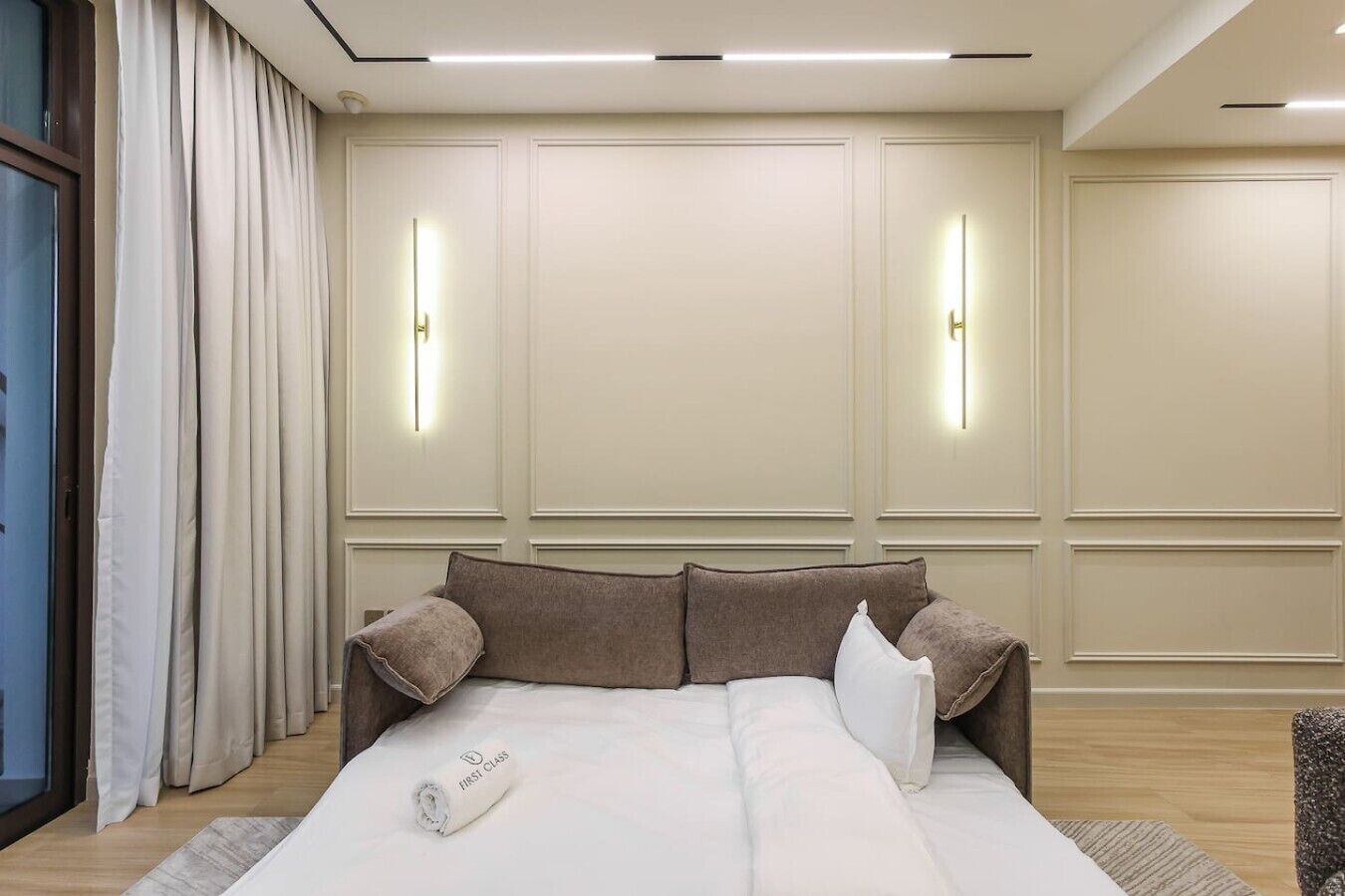 Una habitación de hotel con cama, ventana con cortinas e iluminación en la pared.