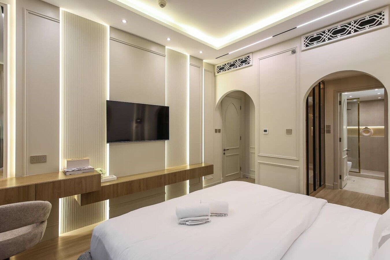 A modern hotel room with a large bed, a flat-screen TV, a desk with a chair, and a shower area.