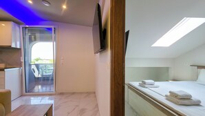 Una camera d'hotel moderna con un letto, una TV, un balcone e un'area ristorazione.