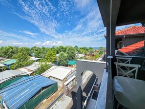 Ein Balkon mit Blick auf eine Wohngegend, darunter Häuser mit unterschiedlichen Dachfarben und einem klaren Himmel.