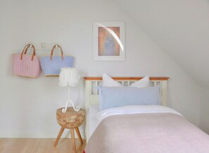 Ein Schlafzimmer mit einem Bett, einer Wandablage mit zwei Handtaschen, einem kleinen hölzernen Hocker und einem gerahmten Bild an der Wand.