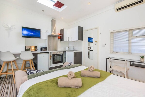 Une chambre d’hôtel moderne équipée d’un lit, d’un bureau, d’une kitchenette et d’un téléviseur.