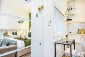 A modern hotel room with a bed, bedside table, and a small seating area with a glass table and chair. - Studio Retreat in Islington (Greater London)