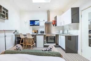 A compact hotel room with a bed, a kitchenette, a TV, and a small bar area.