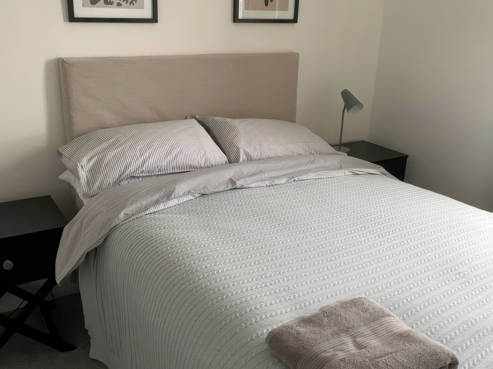 A neatly made bed with a striped pillow, a plain pillow, and a folded blanket on the floor.