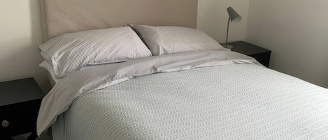 A neatly made bed with a striped pillow, a plain pillow, and a folded blanket on the floor.
